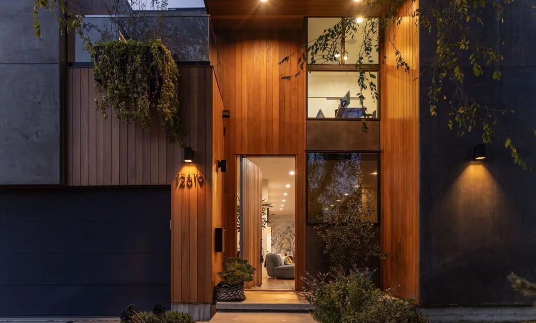 Front door set in vertical wood cladding, lit at dusk