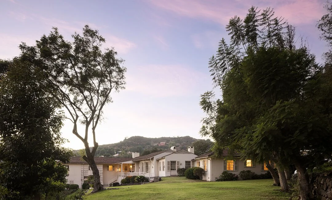 Single-story house beyond a lawn and mature trees